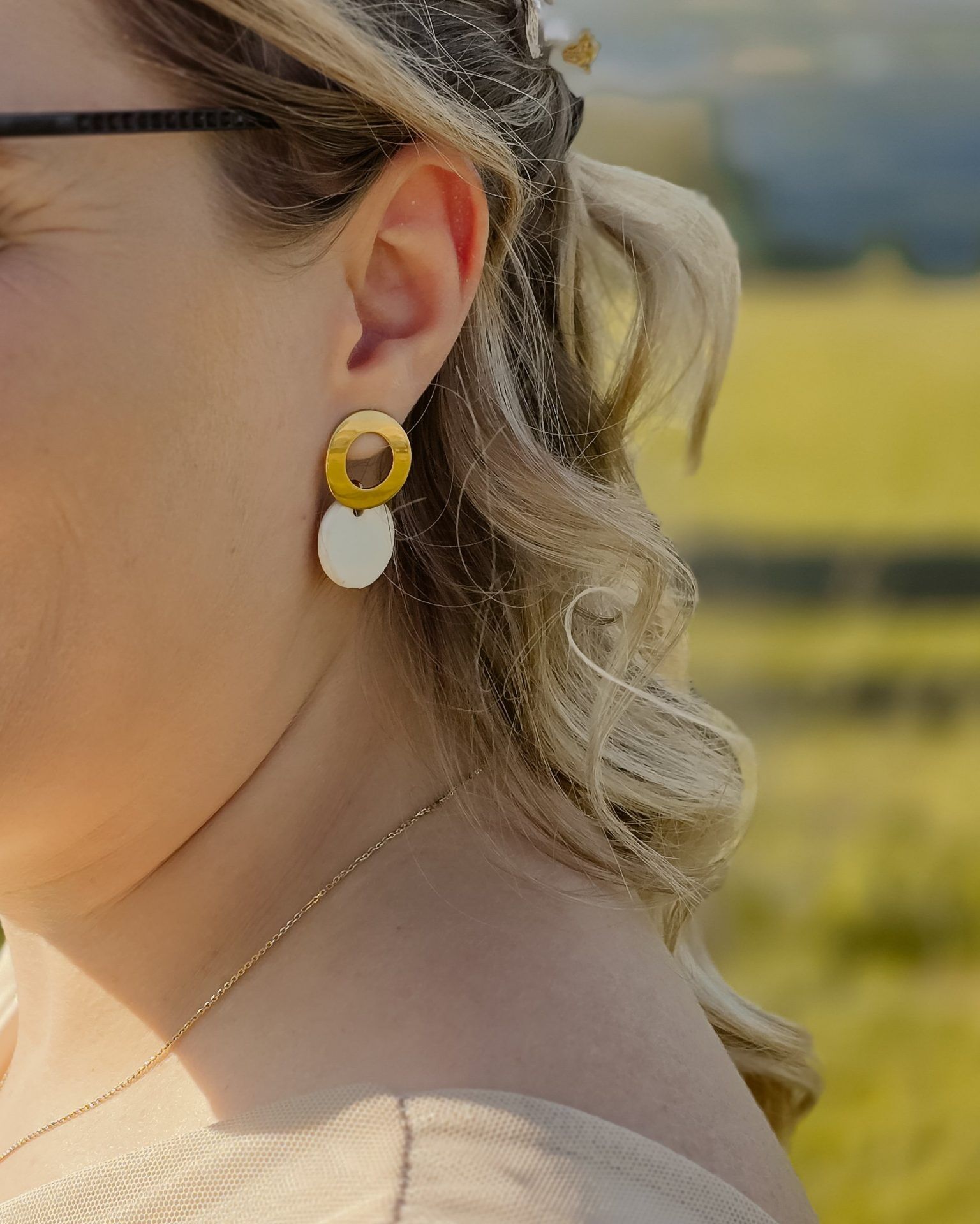 Handgemachte Keramik-Ohrringe in Weiß mit goldfarbenem Edelstahlstecker, antiallergisch, modernes Design getragen von einer Frau mit blond melierten Haaren